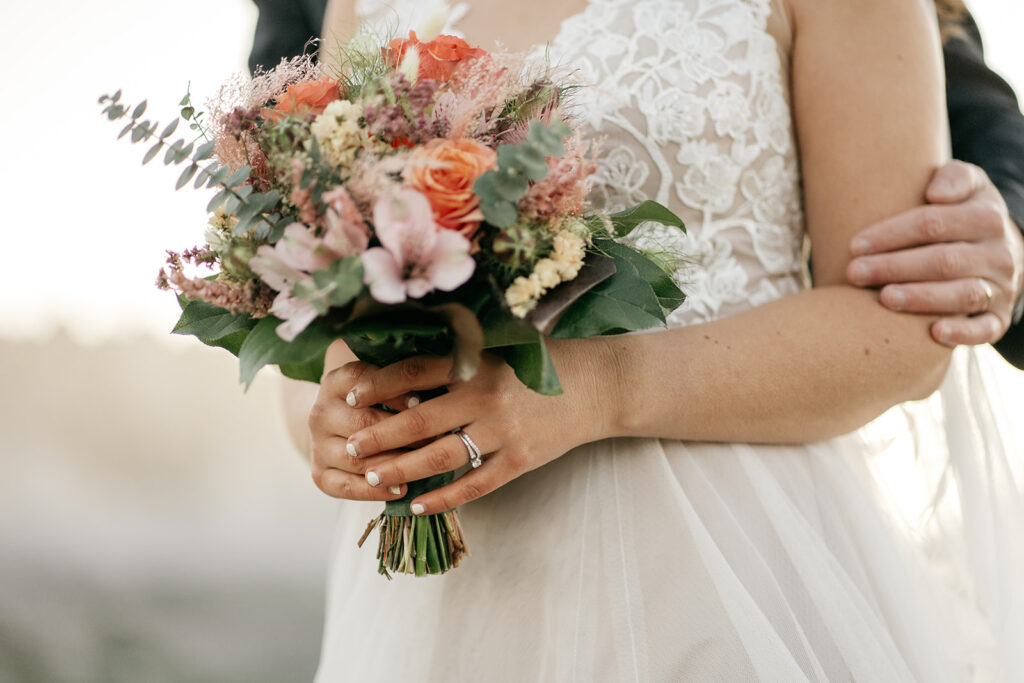 Bride holding colorful wedding bouquet with lace dress.