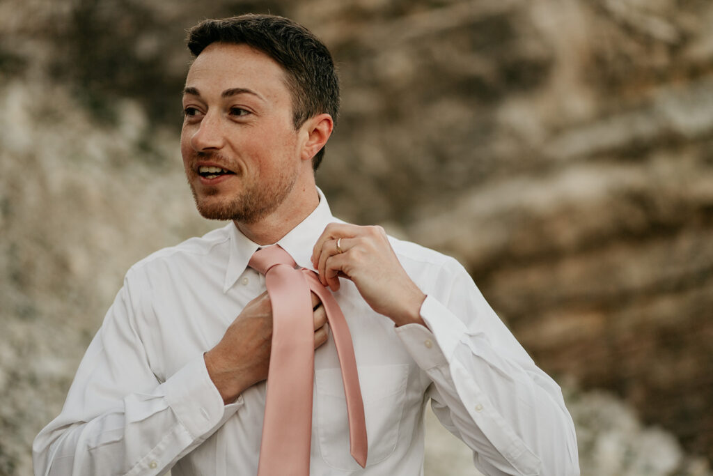 Man adjusting pink tie outdoors.