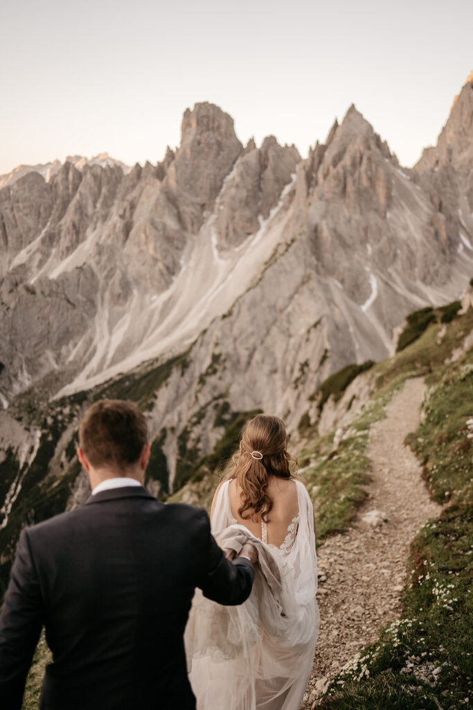 Couple hiking along mountain trail in wedding attire.