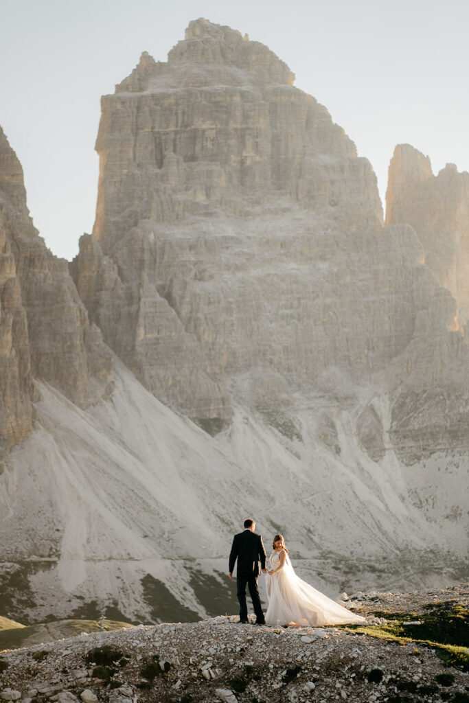 Couple in wedding attire by majestic mountain cliffs.