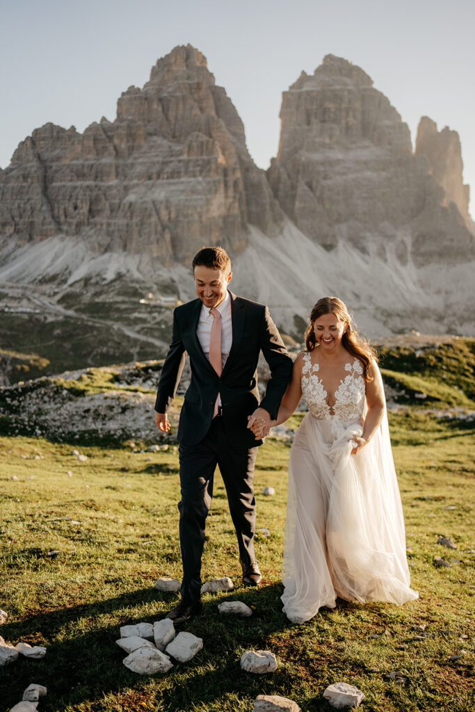 Bride and groom walking in mountain landscape during sunset.