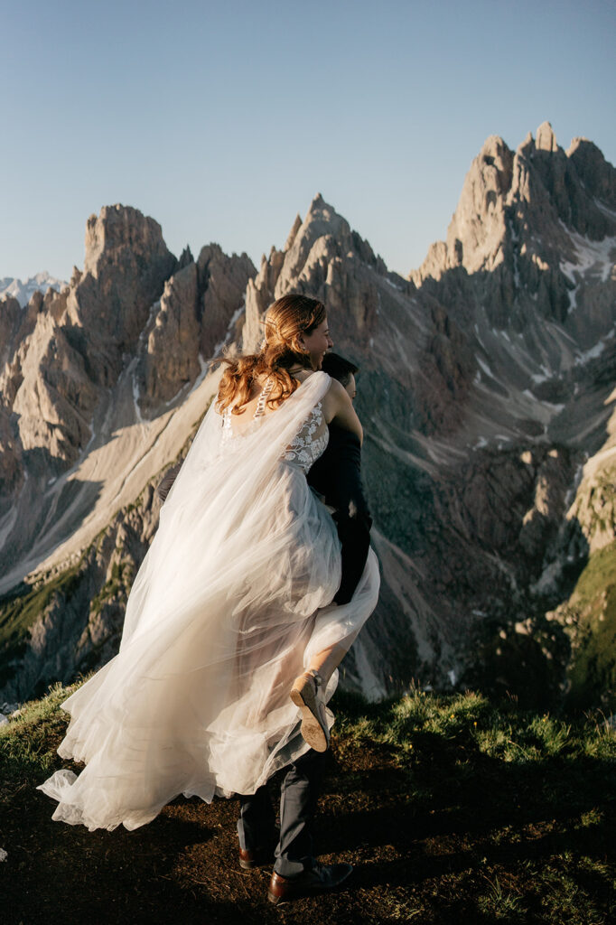 Couple embraces on mountain with wedding attire.