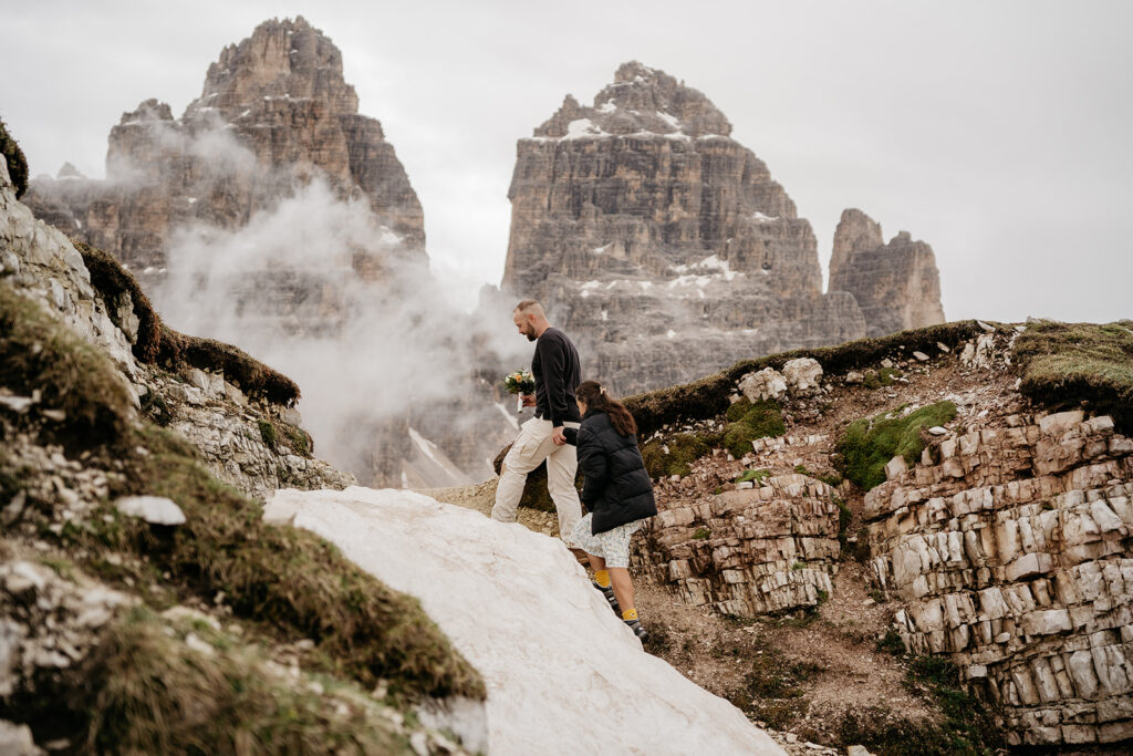 Couple hiking rocky mountain with misty peaks background.