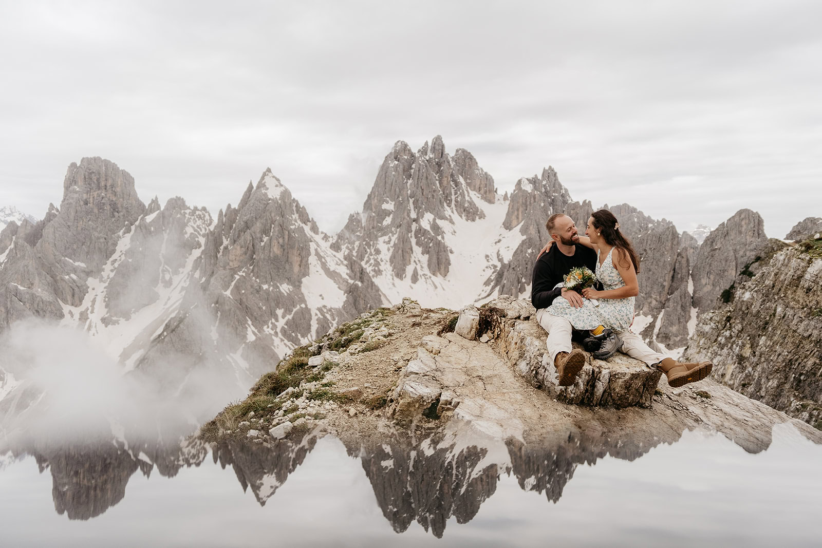 Couple sitting on mountain peak with reflection lake.