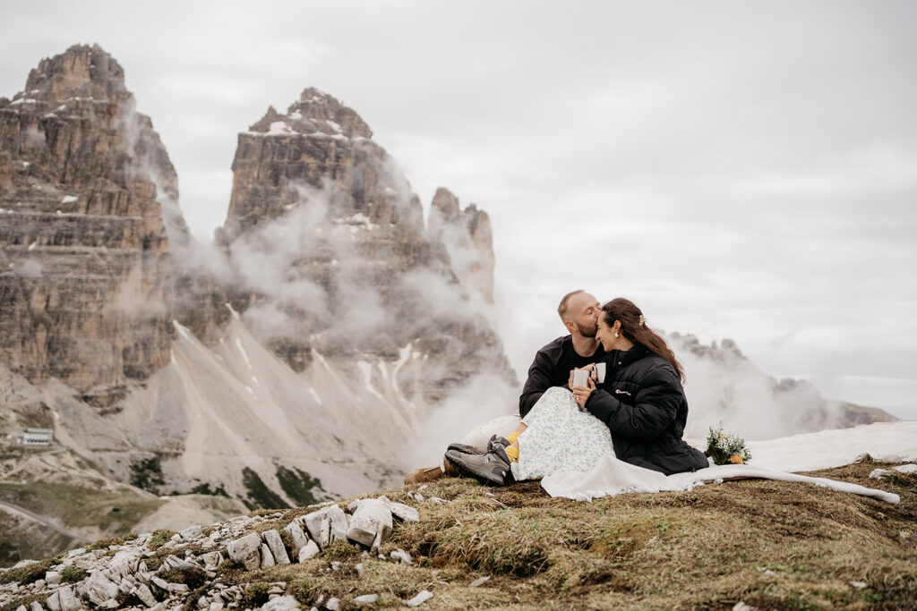 Couple kissing on a mountain picnic blanket.