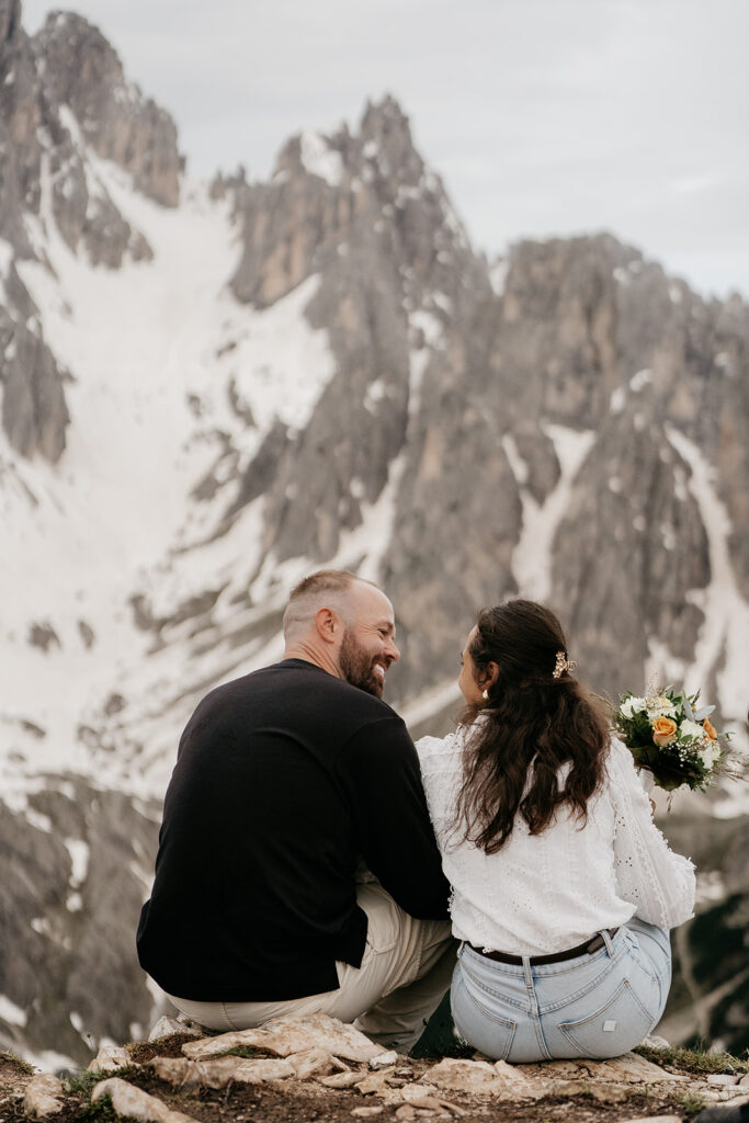 Couple sitting on mountain, smiling at each other.