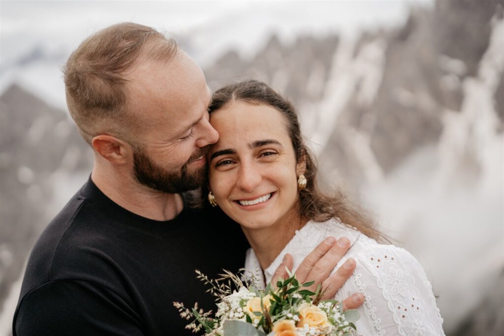 Happy couple embracing with bouquet in mountains