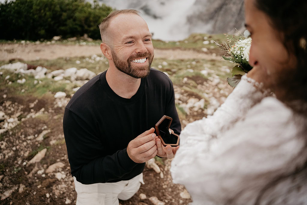 Man proposing with ring outdoors, smiling.