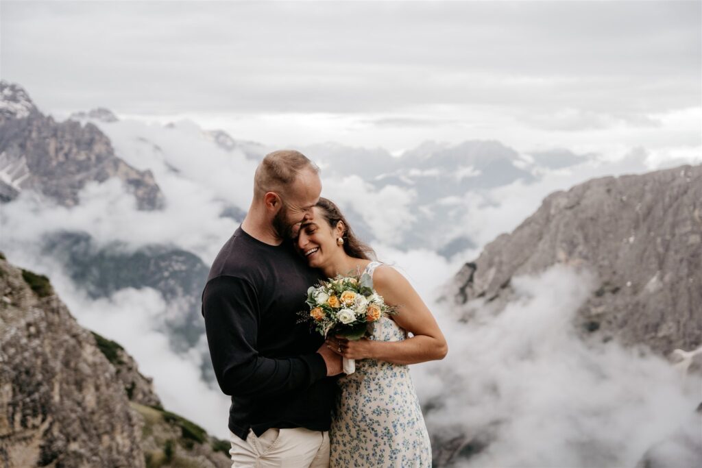 Couple embraces on cloudy mountain landscape.