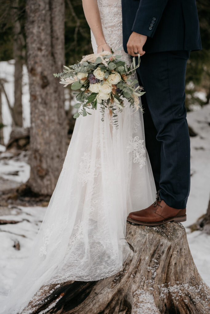 Bride and groom standing on snowy tree stump