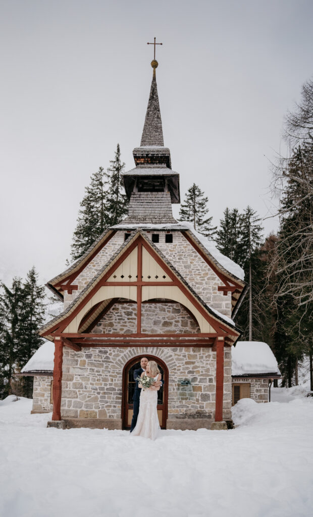 Couple in front of snowy chapel.