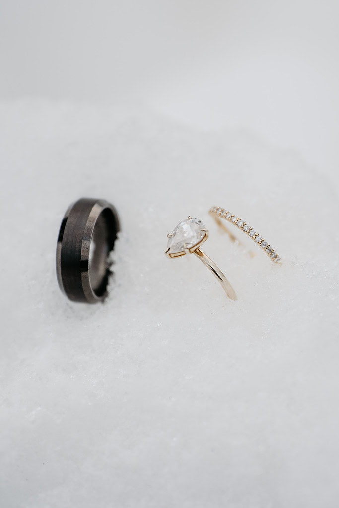 Three rings on snow: black, diamond, and gold bands.