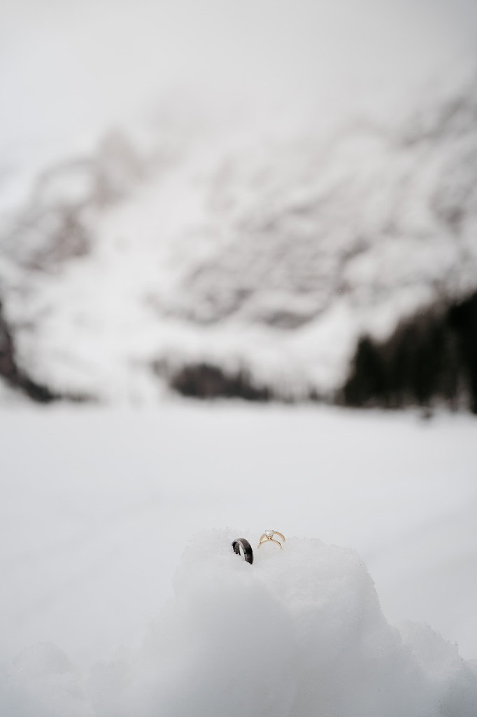 Wedding rings in the snow with blurred mountains.