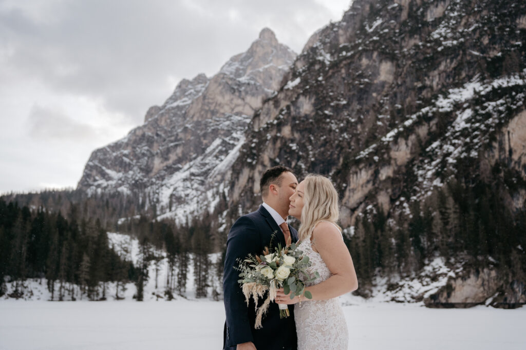 Bride and groom kissing in snowy mountain landscape.