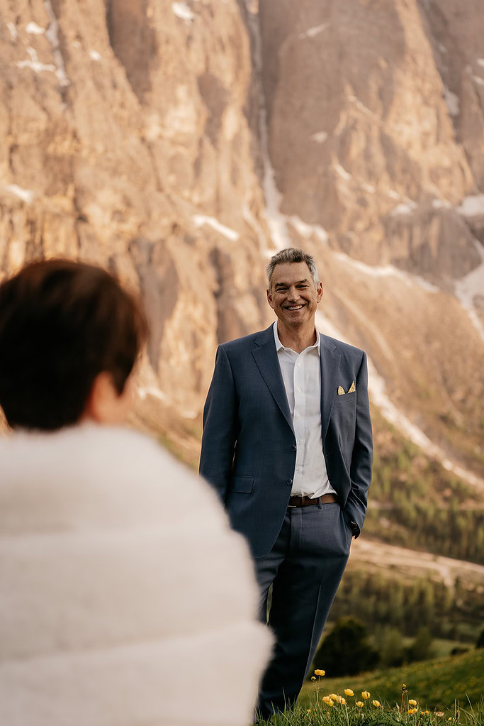 Man in suit smiling near mountain landscape.