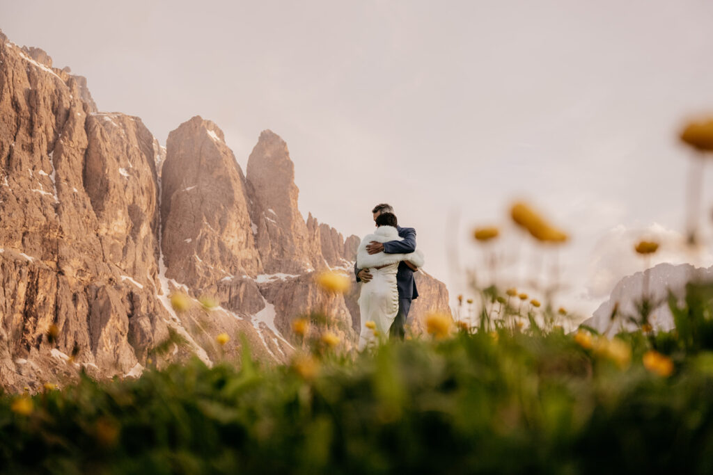 Couple embraces by rocky mountain and wildflowers.