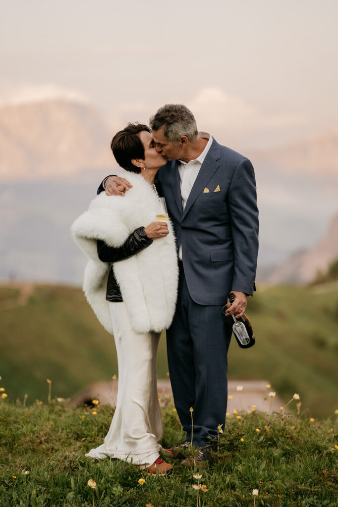 Elderly couple kissing outdoors with champagne bottle.