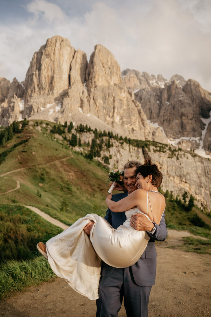 Couple embracing in mountains, wedding dress visible.