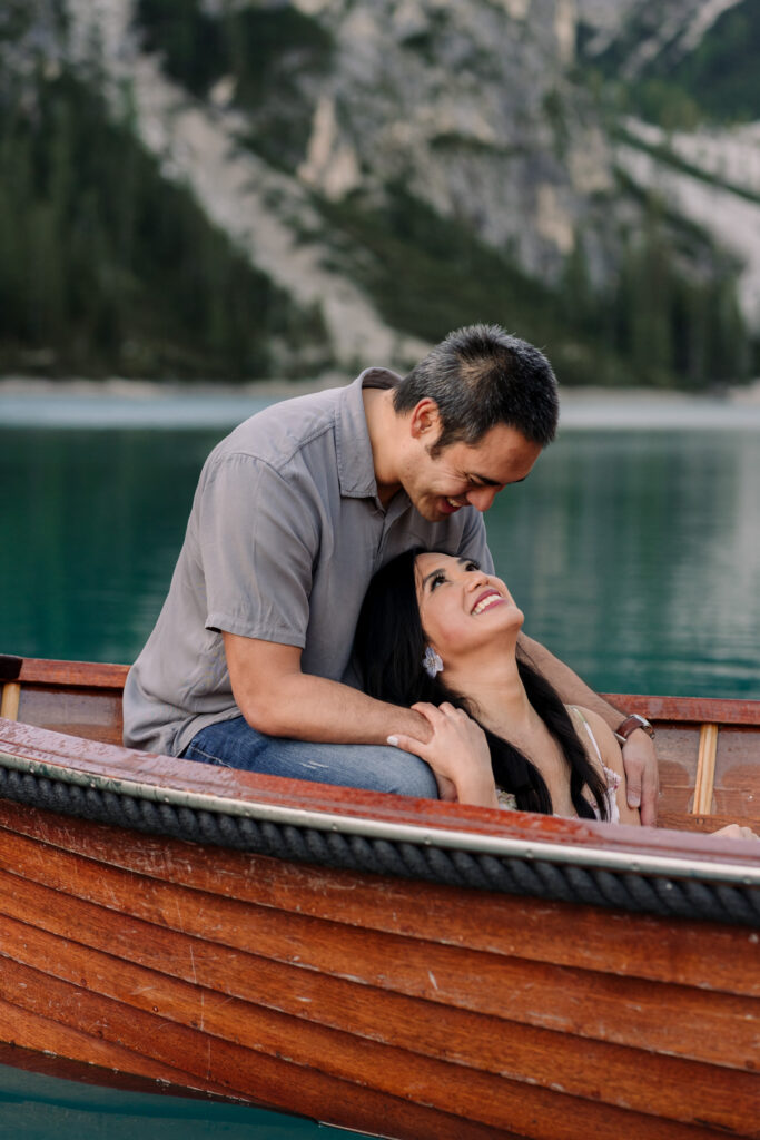 Couple smiling in a wooden boat on a lake.