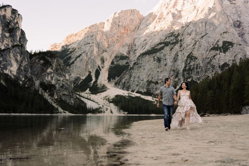 Couple walking on a sandy beach by mountains.