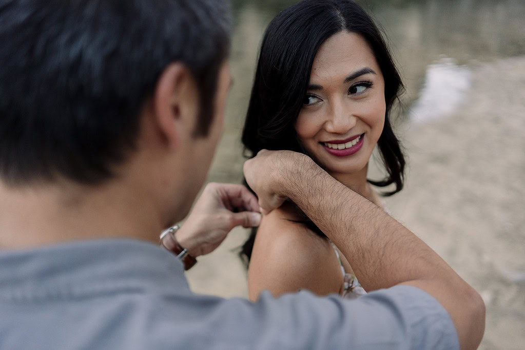 Man helps woman with necklace by water