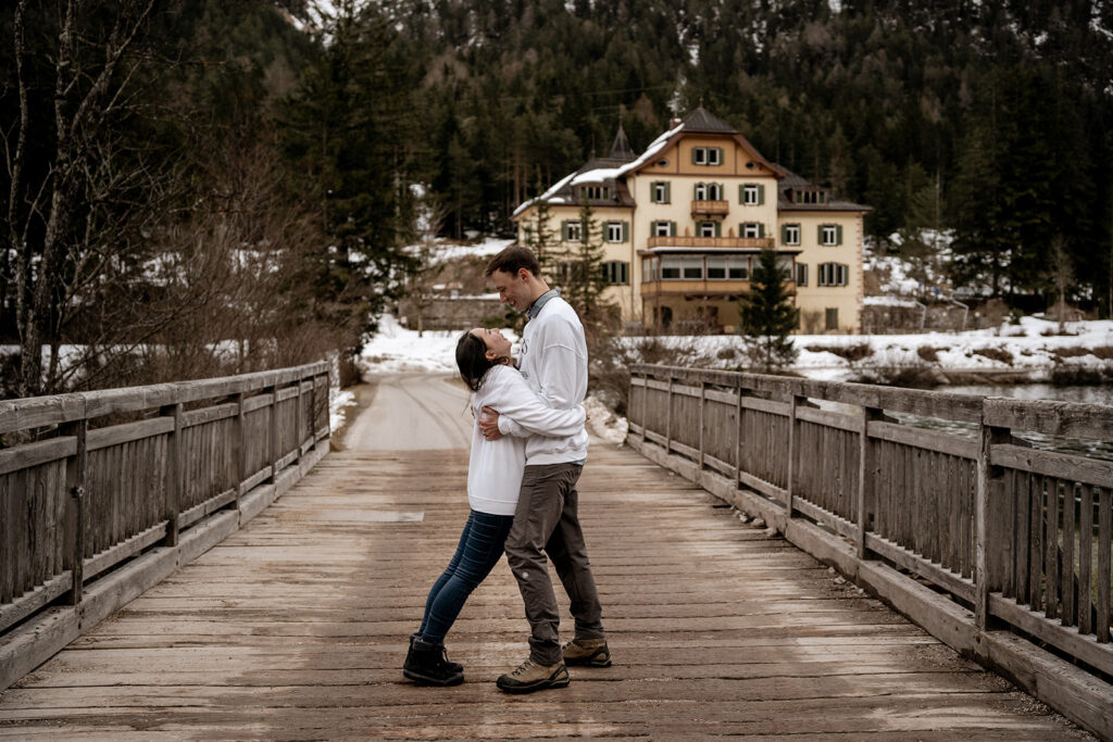 Couple embracing on snowy wooden bridge.