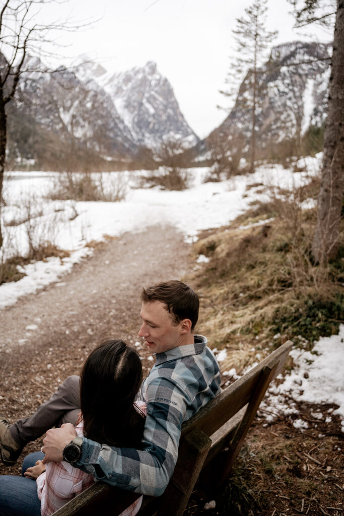 Couple sitting on bench with snowy mountain view.