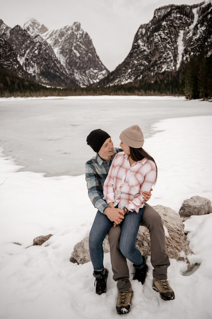 Couple sitting on snowy mountain rocks, smiling.