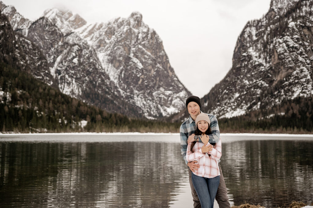 Couple hugging by snowy mountain lake.