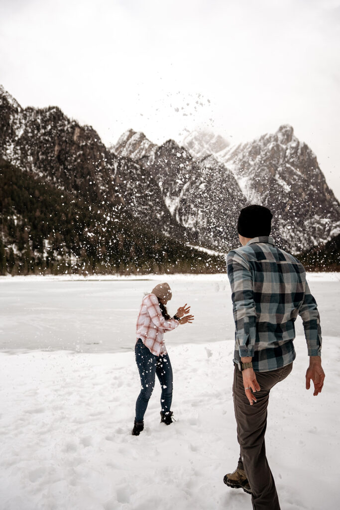 Couple playfully throwing snow in mountain scenery.