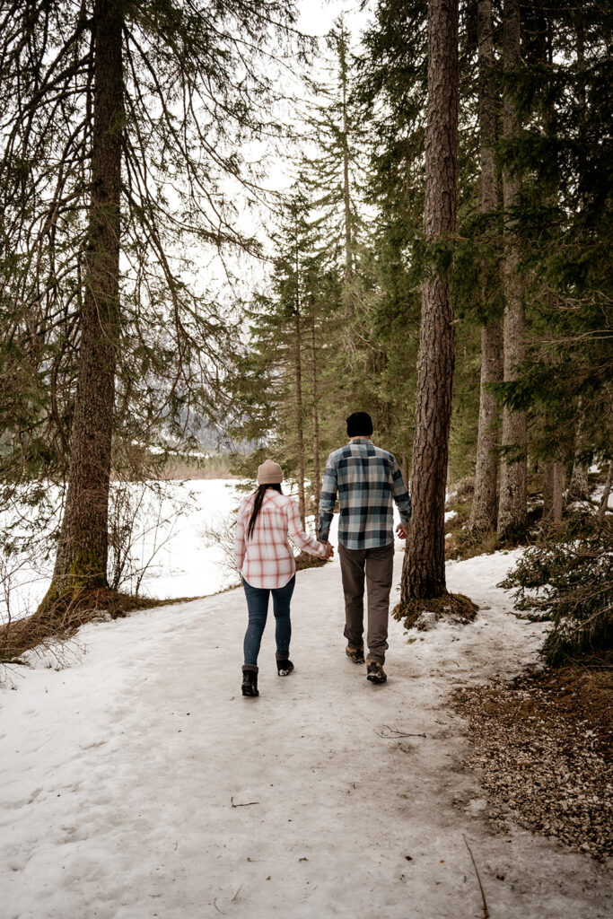 Couple walking hand in hand through snowy forest.