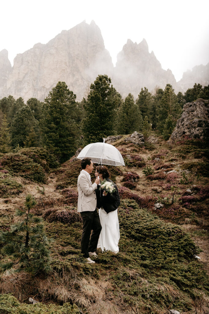 Couple under umbrella in misty mountain landscape.