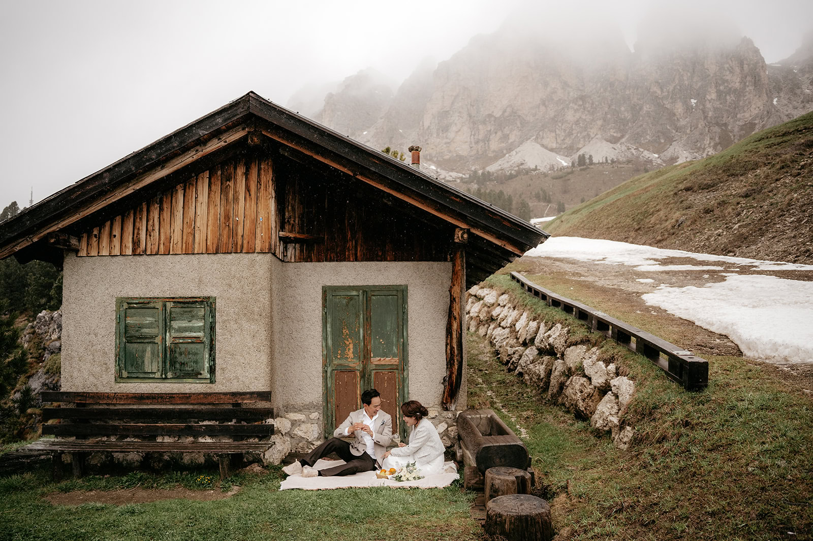 Couple enjoys picnic by rustic cabin in mountains.