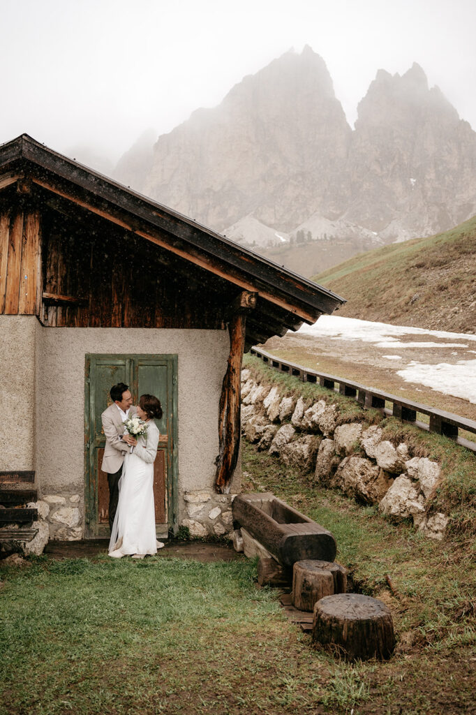 Couple kissing by rustic cabin and mountains.