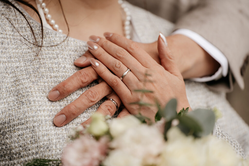 Close-up of wedding rings and hands with flowers.