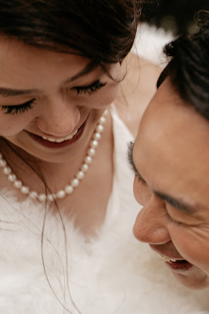 Couple smiling closely together, wearing pearl necklace.