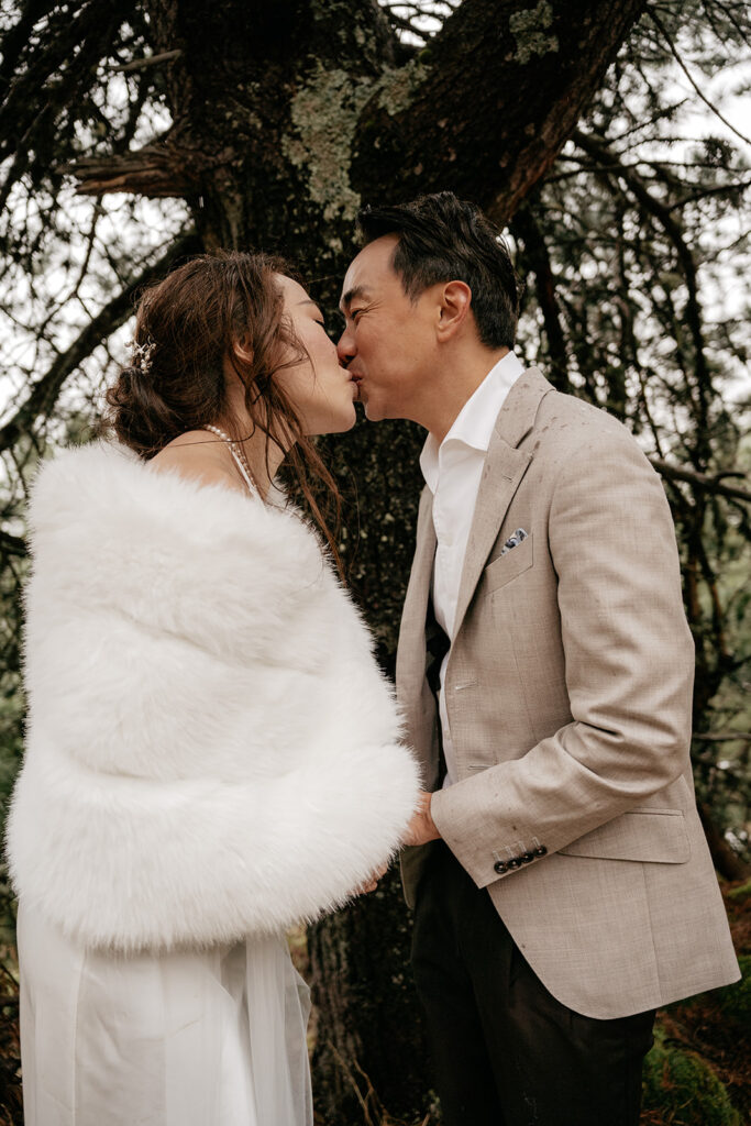 Couple kissing under a tree in wedding attire