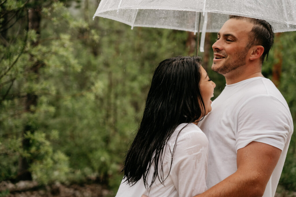 Couple laughing under transparent umbrella in rain