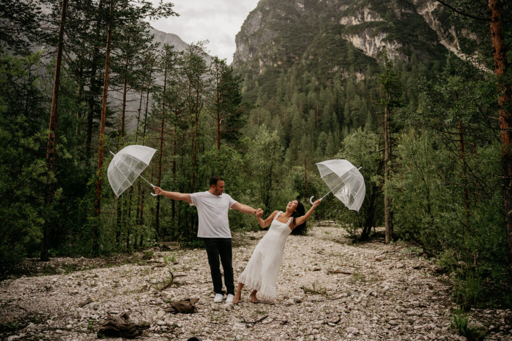 Couple with umbrellas dancing in a forest path.