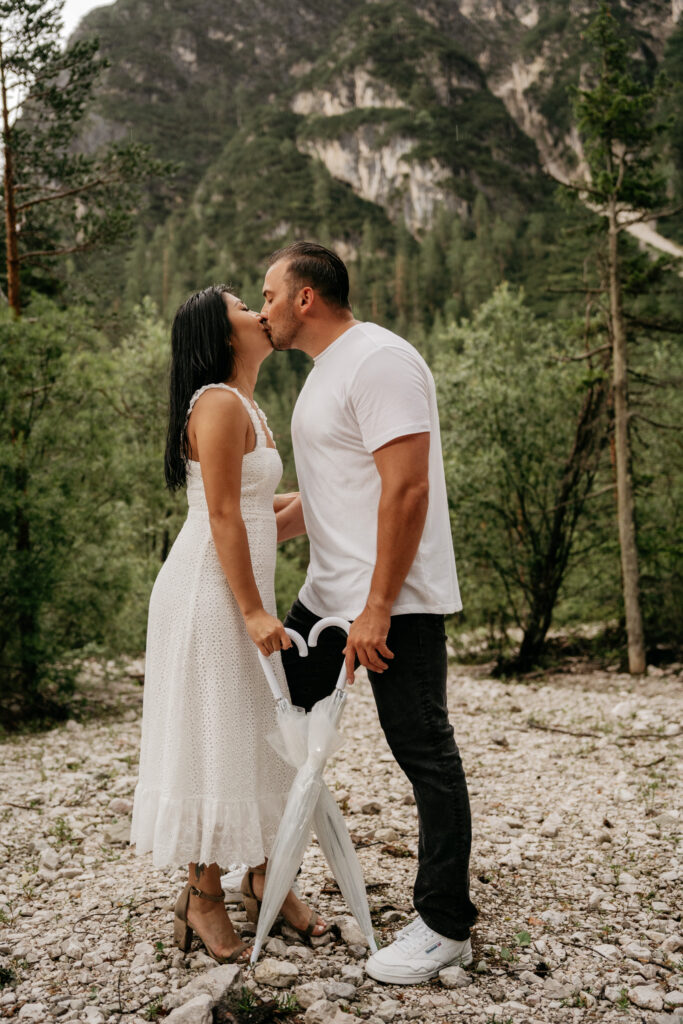 Couple kissing in a forest holding an umbrella.