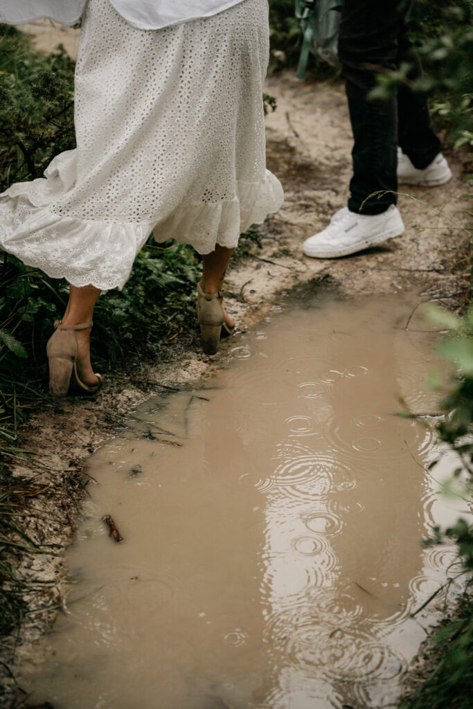 Woman walking near muddy puddle in white dress.