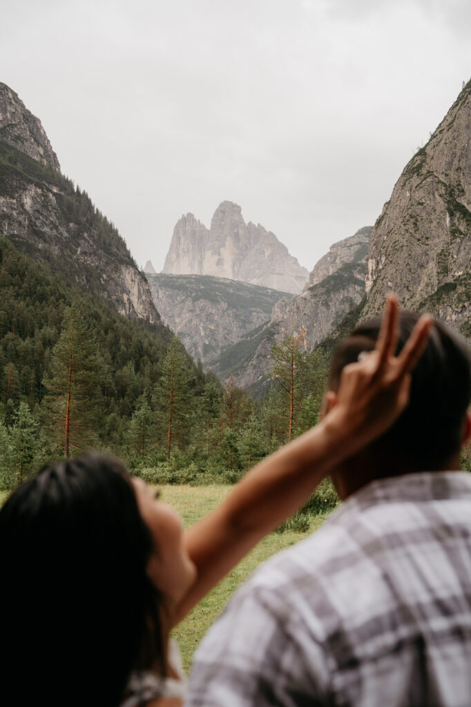 Couple in mountains, woman making peace sign.