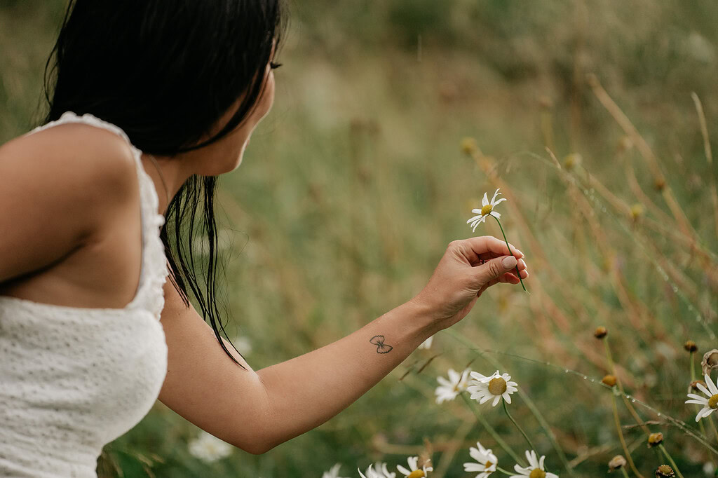 Woman holding daisy in grassy field.