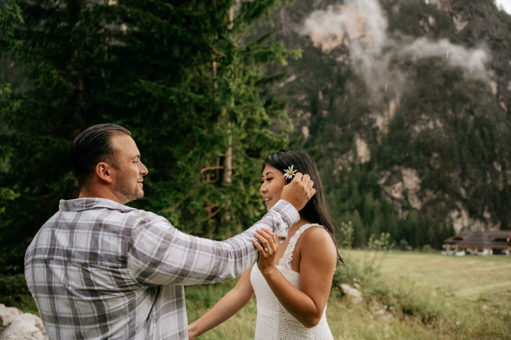 Man placing flower in woman's hair, forest background.