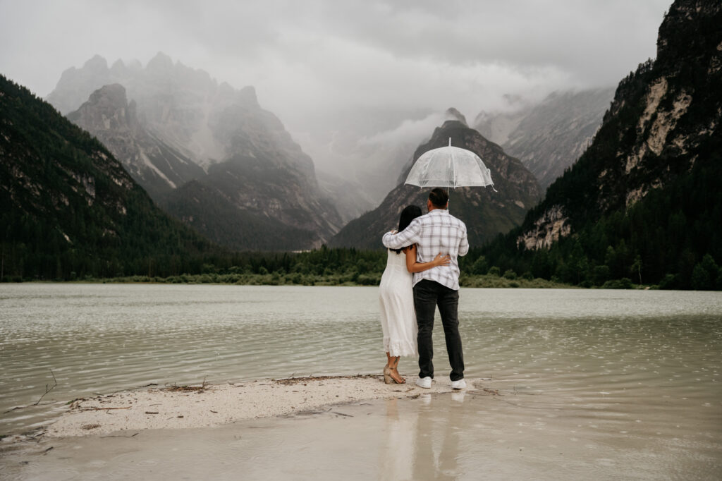 Couple embracing under umbrella by mountain lake.