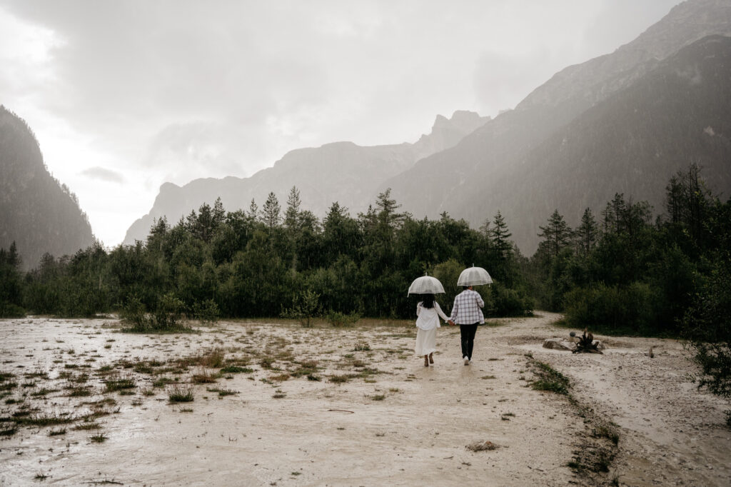 Couple walking with umbrellas in rainy mountain landscape.