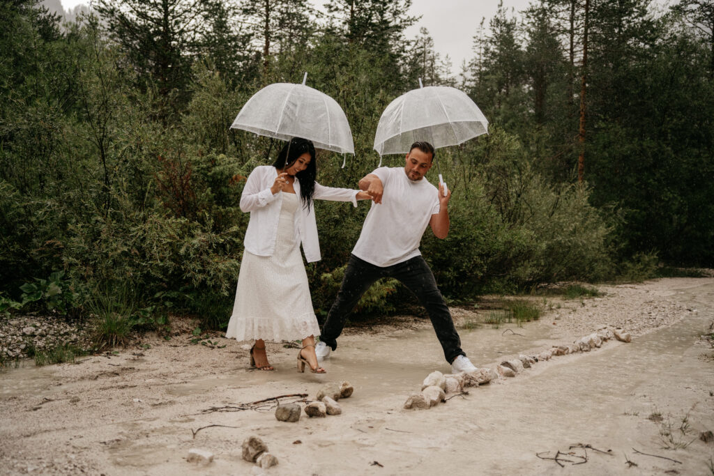 Couple with umbrellas crossing muddy path in forest