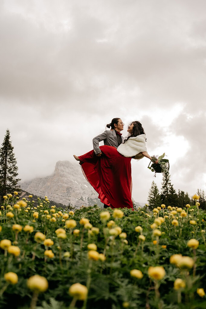 Couple celebrating outdoors with mountains and flowers.