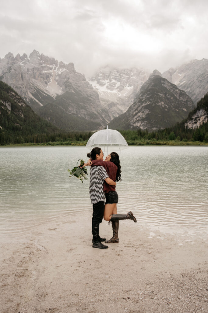 Couple embracing by mountain lake with umbrella.