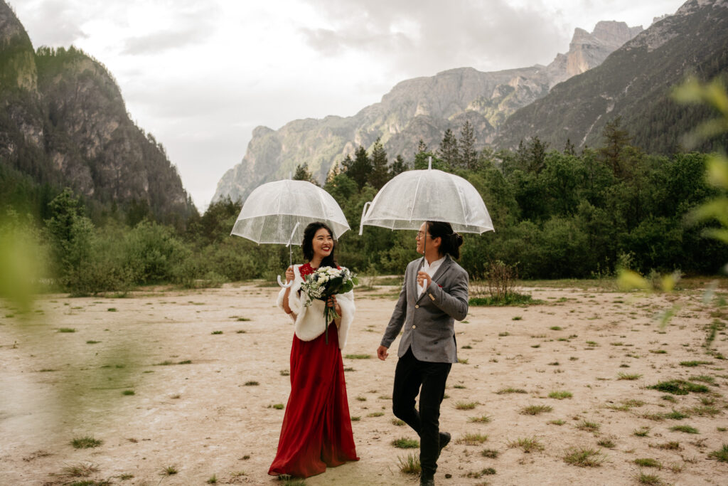 Couple walking with umbrellas in a mountainous landscape.